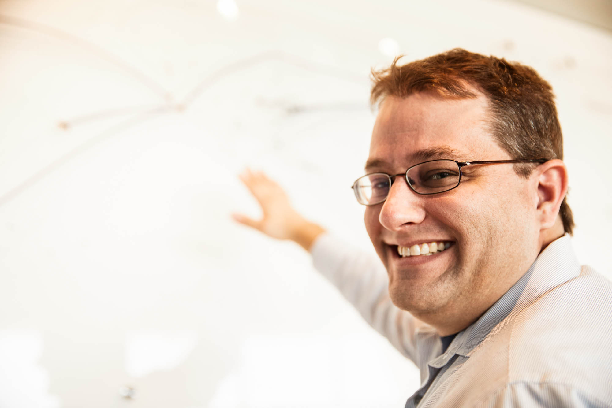 Smiling Boom Supersonic team member with glasses pointing at flight route map display in office