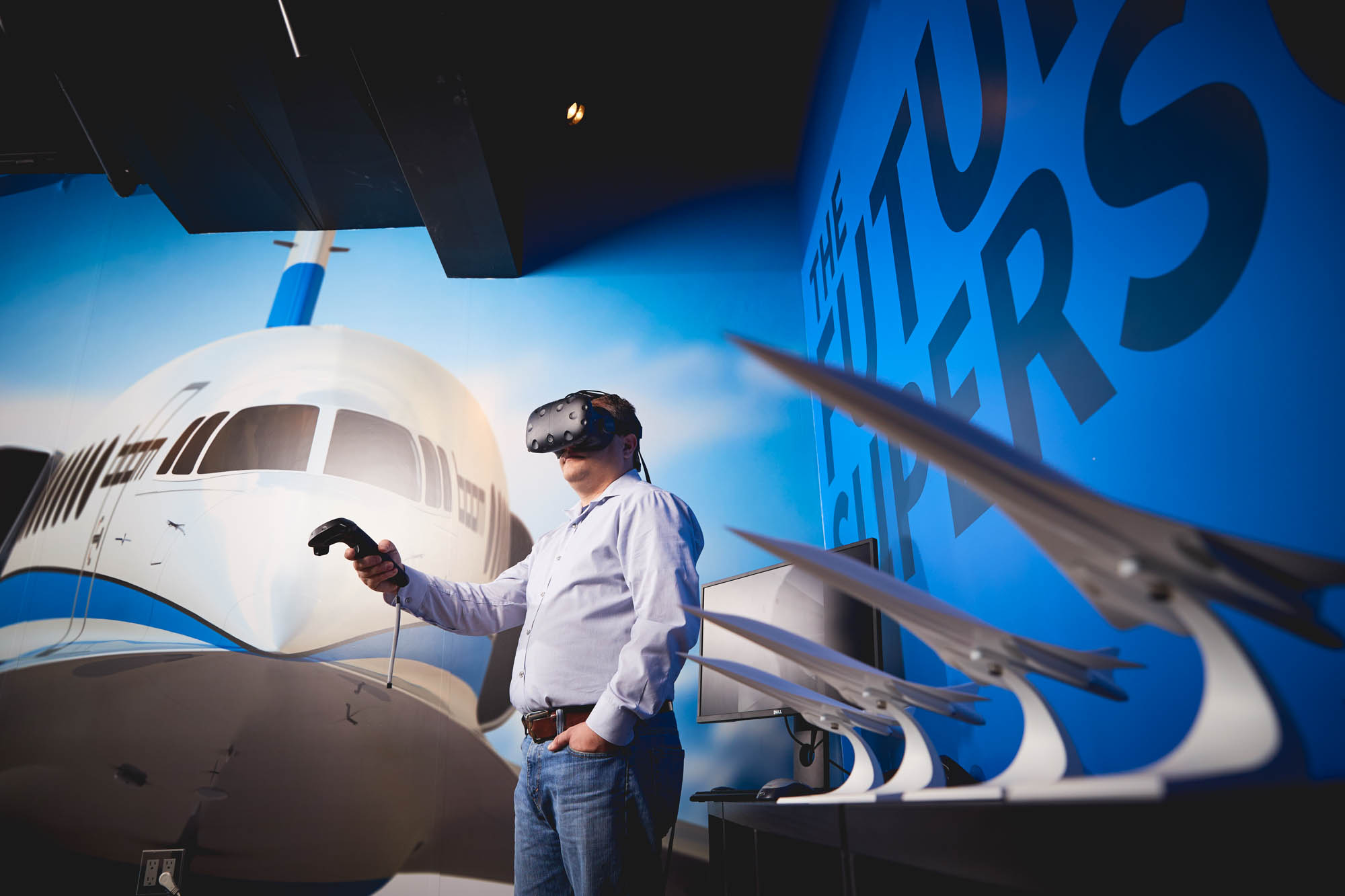 Boom Supersonic team member wearing VR headset using virtual reality controllers in front of supersonic jet mural