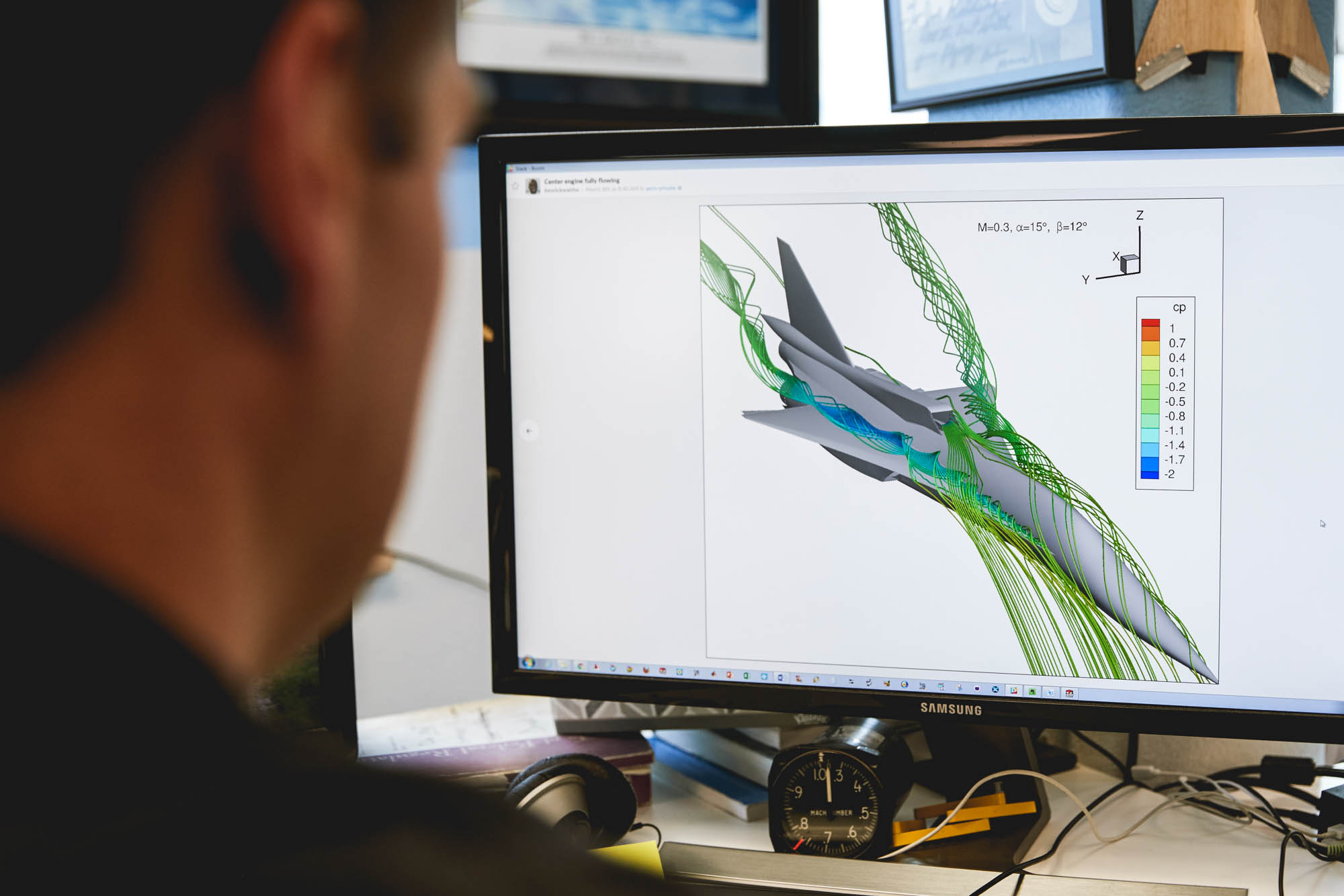 Engineer reviewing a computational fluid dynamics simulation of a supersonic aircraft on a Samsung monitor showing colored pressure coefficient streamlines