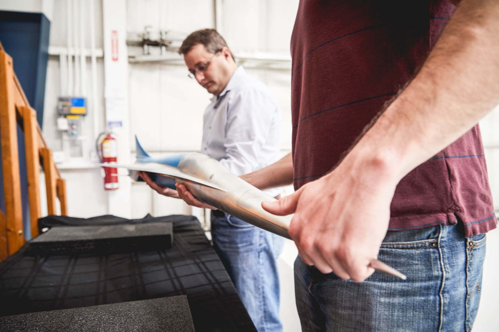 Boom Supersonic engineer in light blue shirt examining model aircraft components held by colleague in workshop