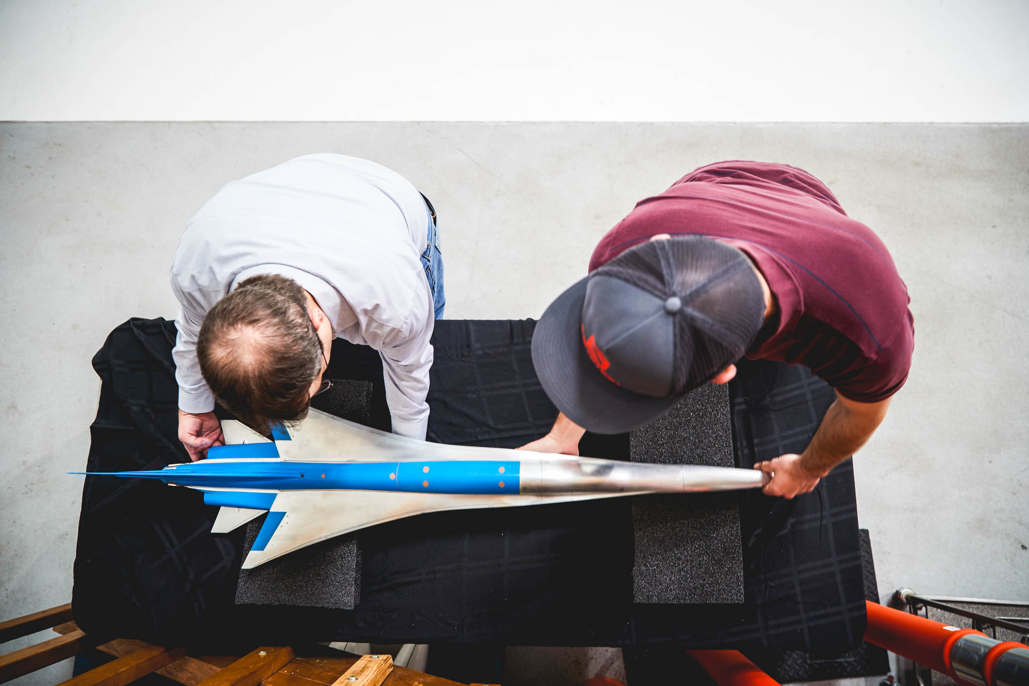 Overhead view of two Boom Supersonic engineers examining a small-scale model of the supersonic passenger jet