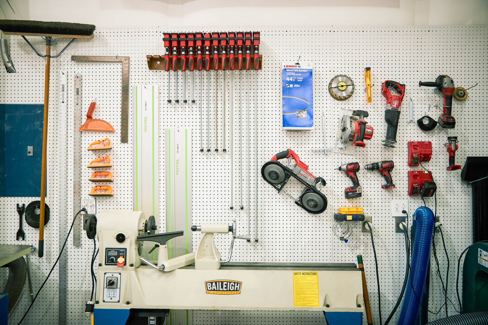 Organized Boom Supersonic workshop pegboard wall hung with red clamps, power tools, drills, and a Baileigh wood lathe below