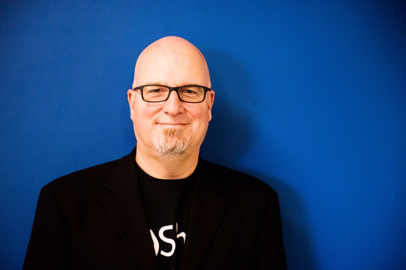 GoShare team member portrait - bald man with glasses and goatee wearing GoShare branded shirt and black blazer