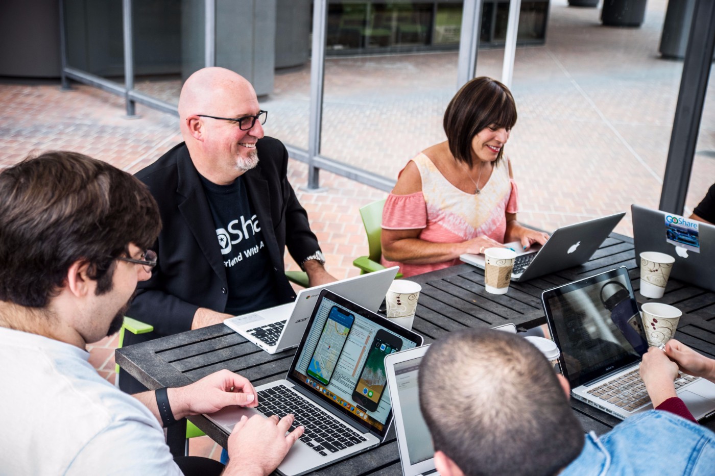 GoShare team meeting outdoors with laptops and coffee cups at a wooden table