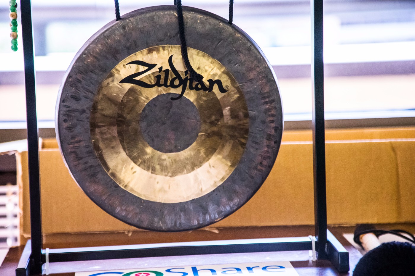 Close-up of GoShare's office Zildjian gong hanging on stand with GoShare logo visible at the bottom