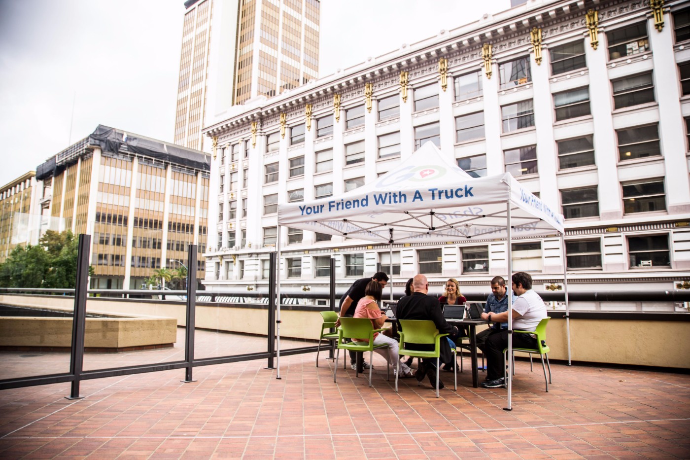 GoShare team meeting under a Your Friend With A Truck branded canopy on a rooftop with downtown buildings