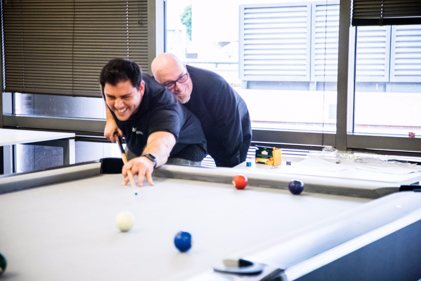 Two GoShare team members playing pool in their San Diego office, one taking a shot while the other watches