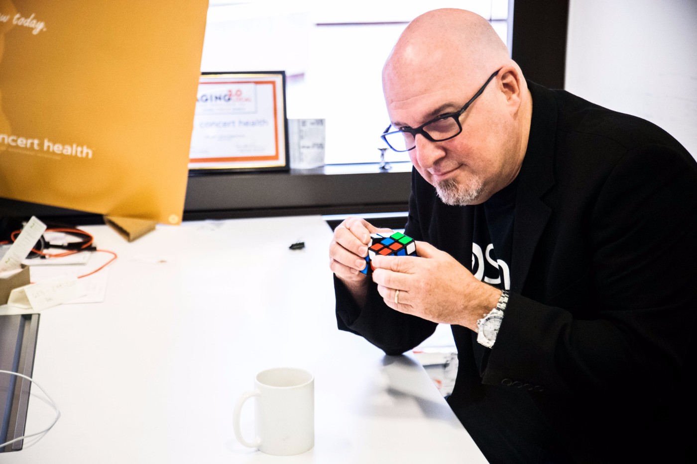GoShare CEO solving a Rubik's Cube at his office desk with concert health awards in background