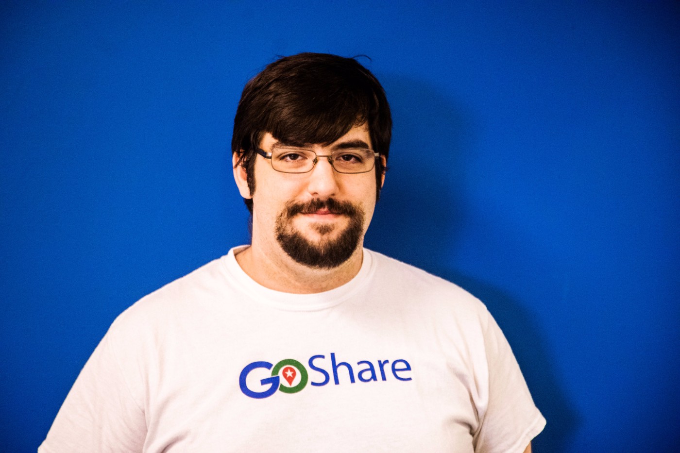 GoShare team member portrait - man with glasses and goatee wearing white GoShare branded t-shirt