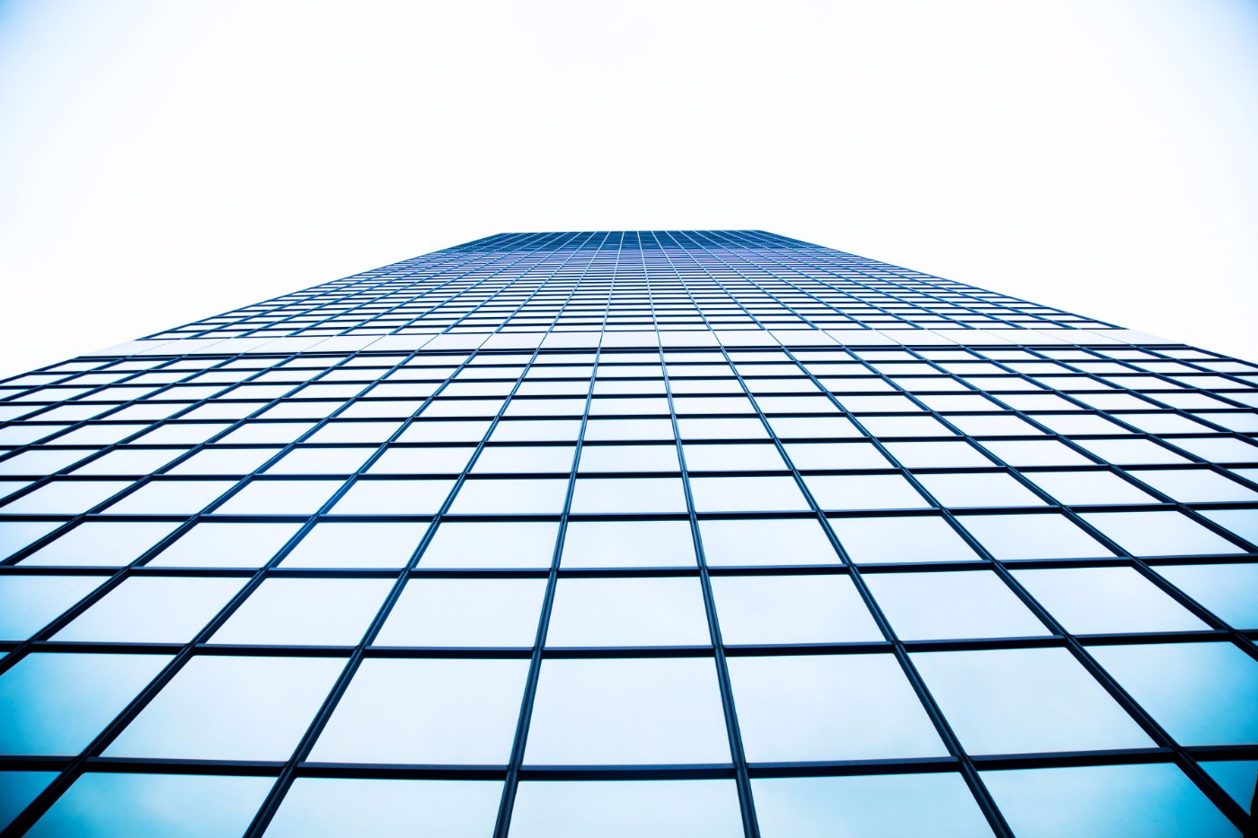Upward perspective view of a glass-walled skyscraper rising into a clear sky
