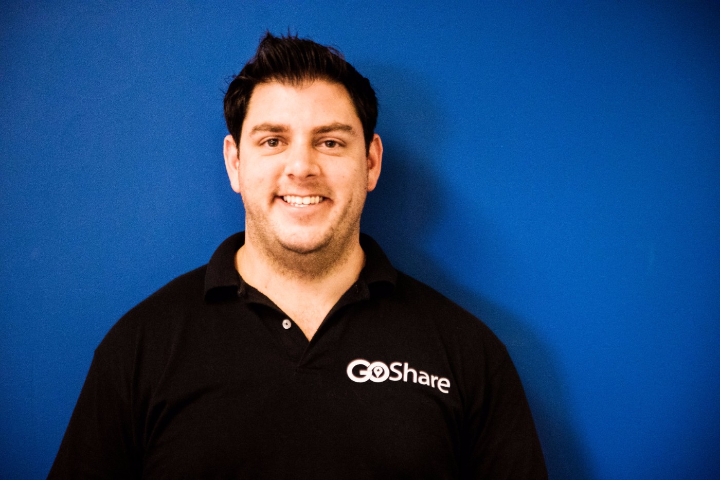 GoShare team member portrait - smiling man with dark hair wearing black GoShare branded polo shirt