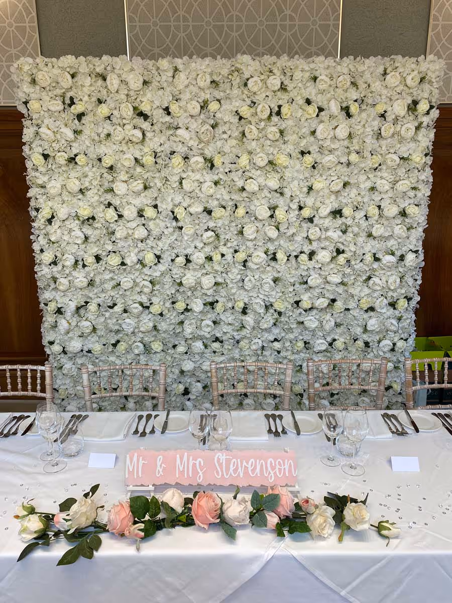 A floral backdrop with a table set for a wedding, reads "Mr & Mrs Stevenson."