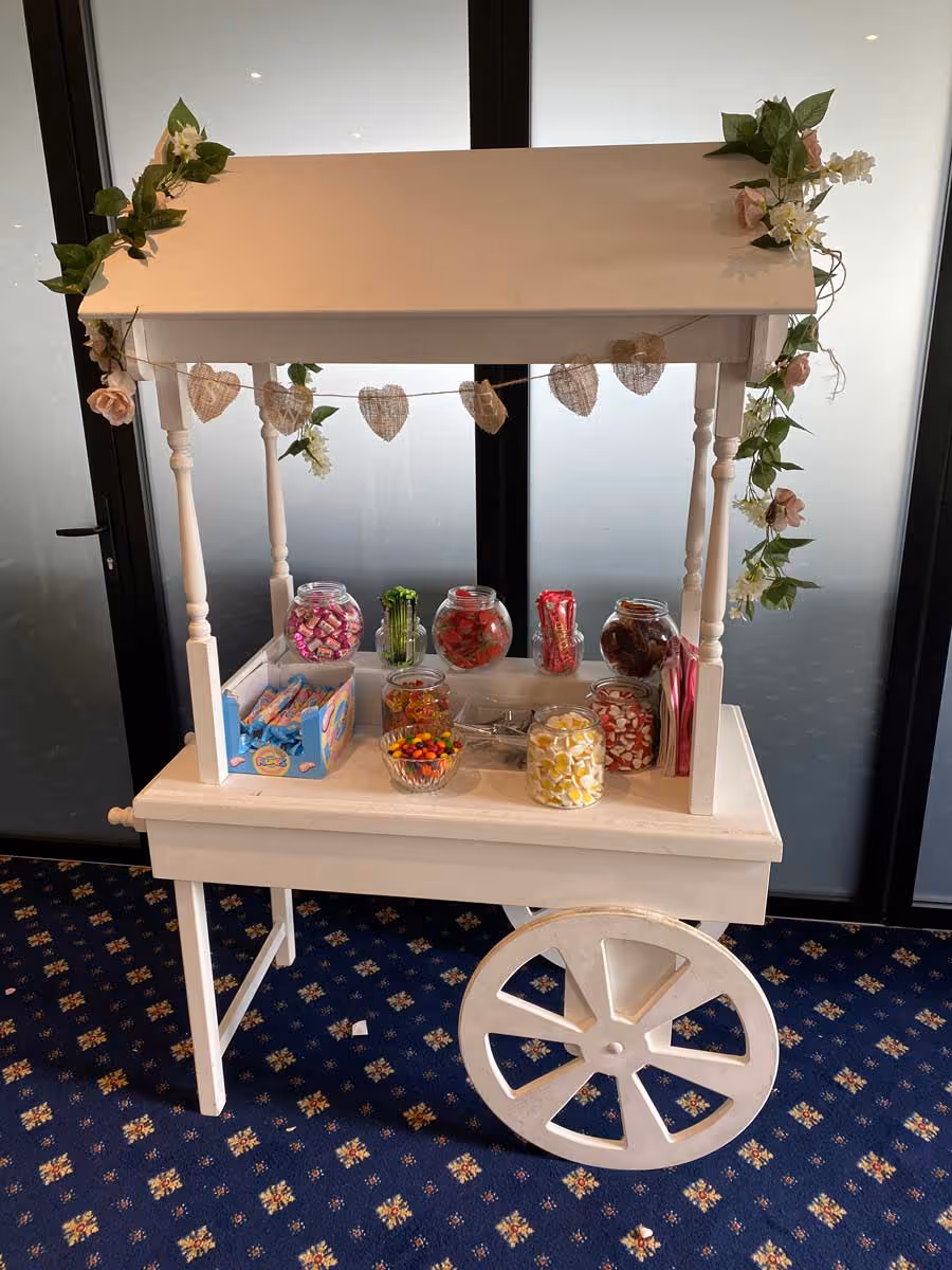 A white candy cart with jars filled with assorted colorful candies is on display.