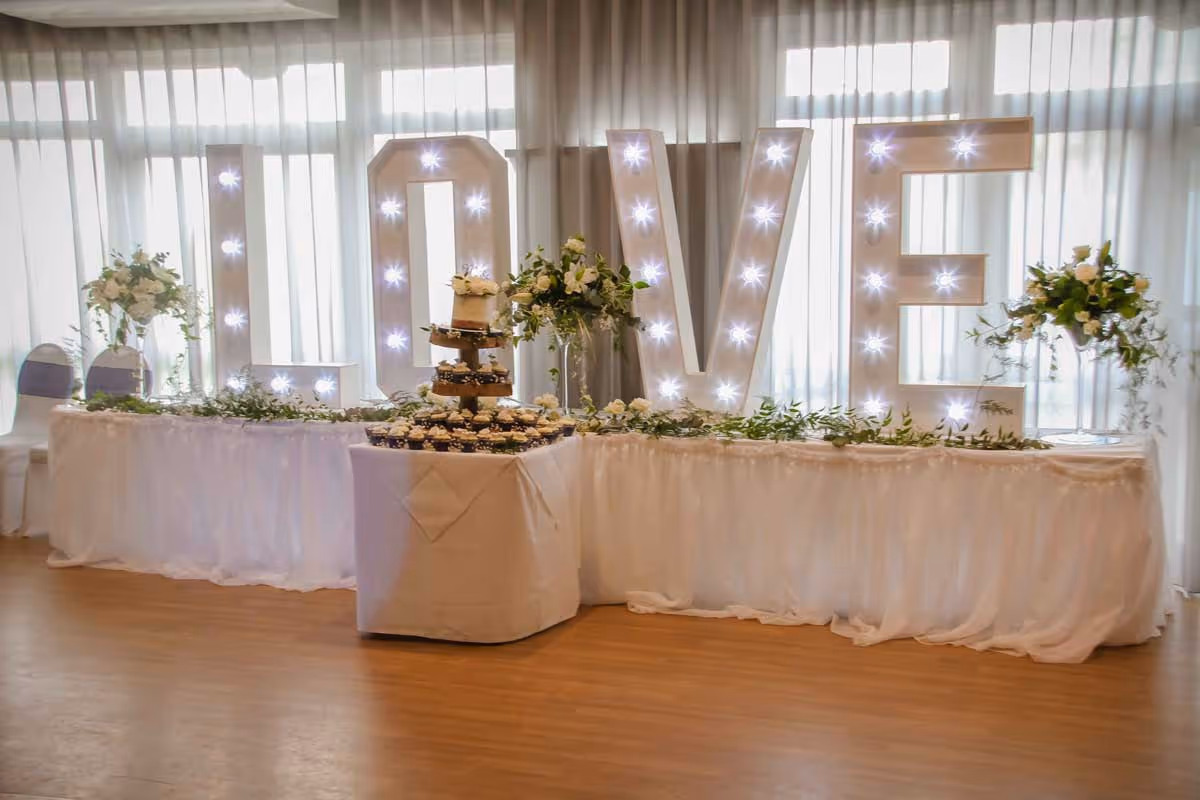 A wedding reception table with large illuminated "LOVE" letters and a tiered cake.