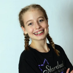 Smiling girl with braces and braided hair wearing a black Stardash Academy shirt against a light background.