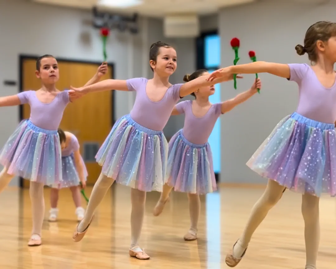 A primary ballet class holding outstretched a rose in colourful skirts.