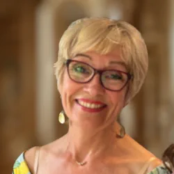 Smiling woman with short blonde hair and glasses wearing yellow earrings and a yellow top.