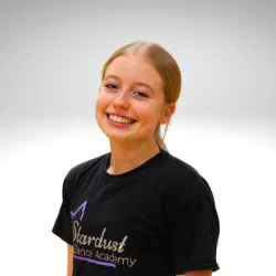 Smiling young woman with blonde hair in a ponytail wearing a black Stardust Dance Academy t-shirt.
