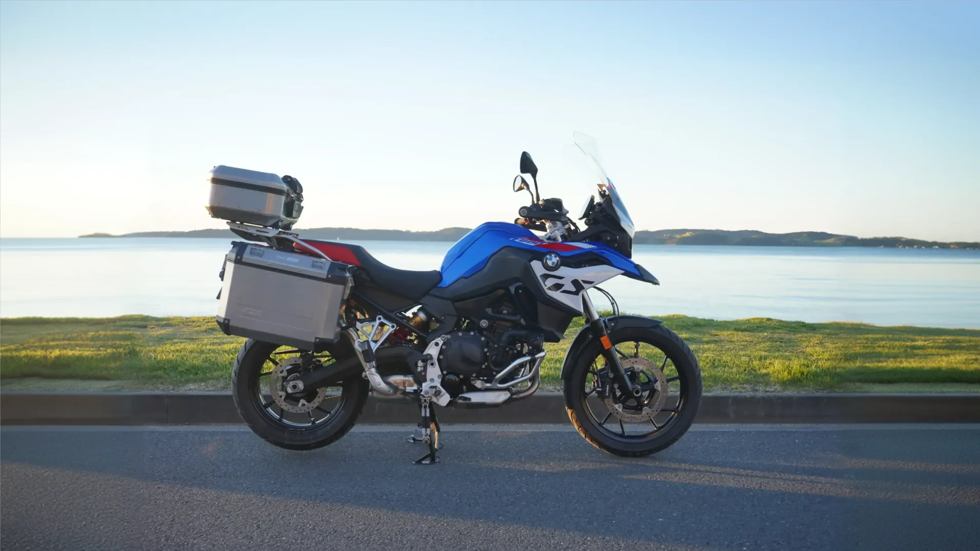 Blue BMW F800 GS with aluminium panniers and top box, parked by the water at sunrise