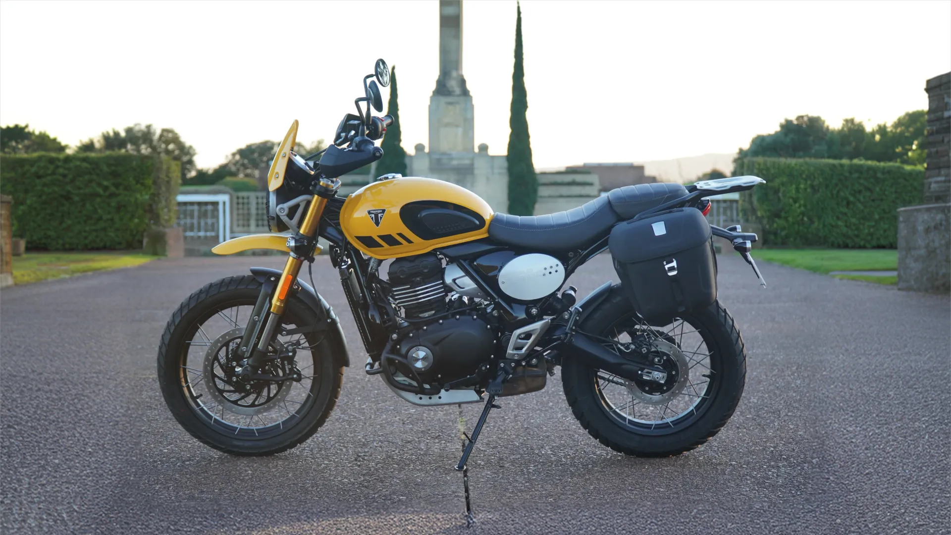 Yellow Triumph Scrambler 400XC with luggage panniers, parked side-on at dusk