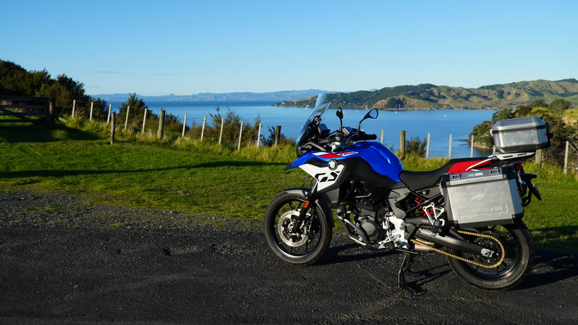 Blue BMW F800 GS with aluminium panniers and top box, parked above a coastal bay in New Zealand