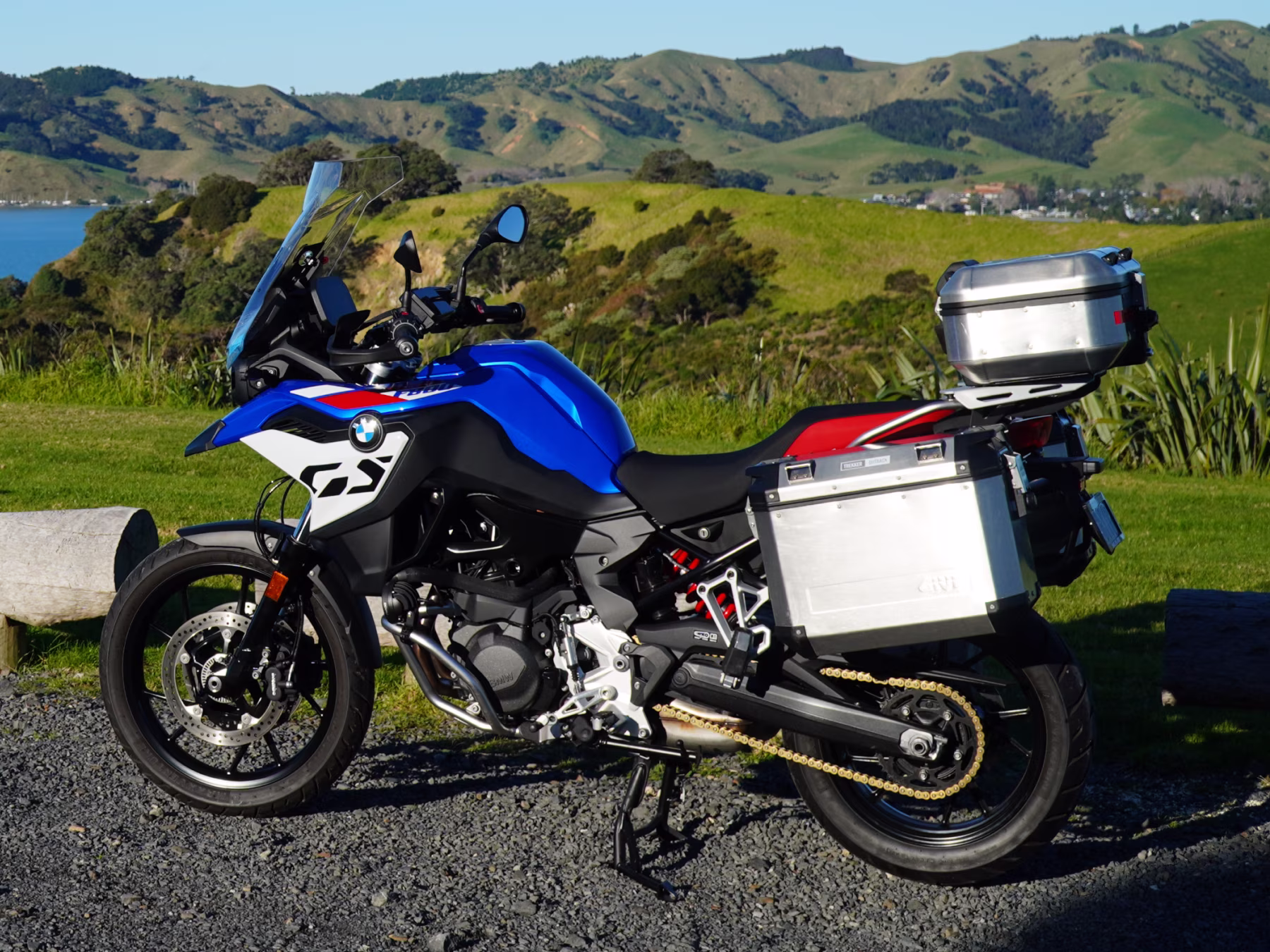 BMW F800 GS in blue, white and red with aluminium GIVI panniers and top box, parked on gravel above a coastal bay