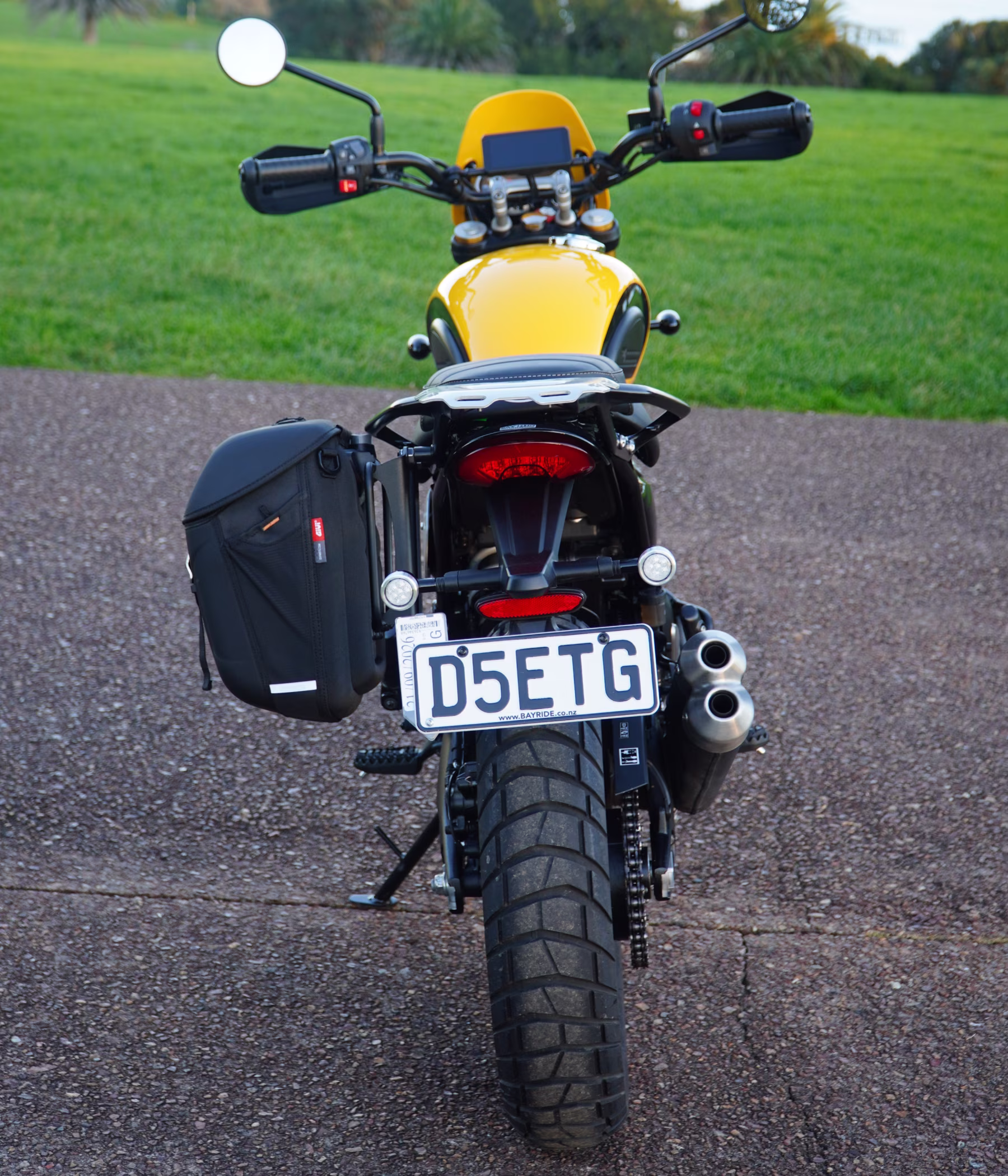 Rear view of the yellow Triumph Scrambler 400XC fitted with a soft pannier and luggage rack, prepared and ready for collection