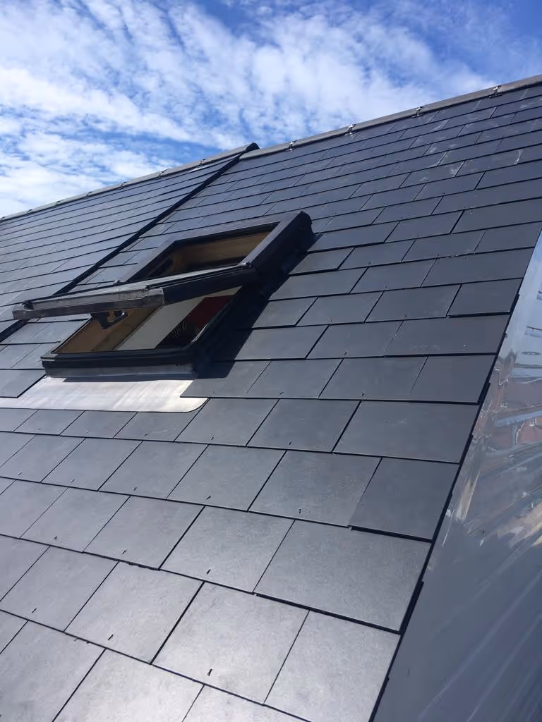An open rooftop window on a slate-tiled roof under a partly cloudy sky.