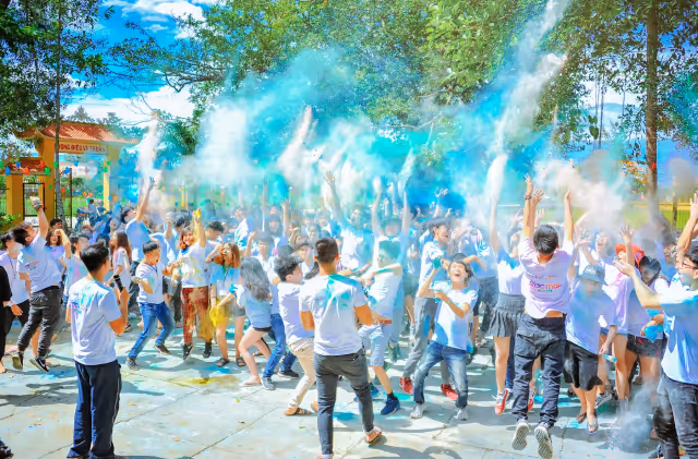 Group of people outdoors throwing blue and white powder in the air during a festive celebration.