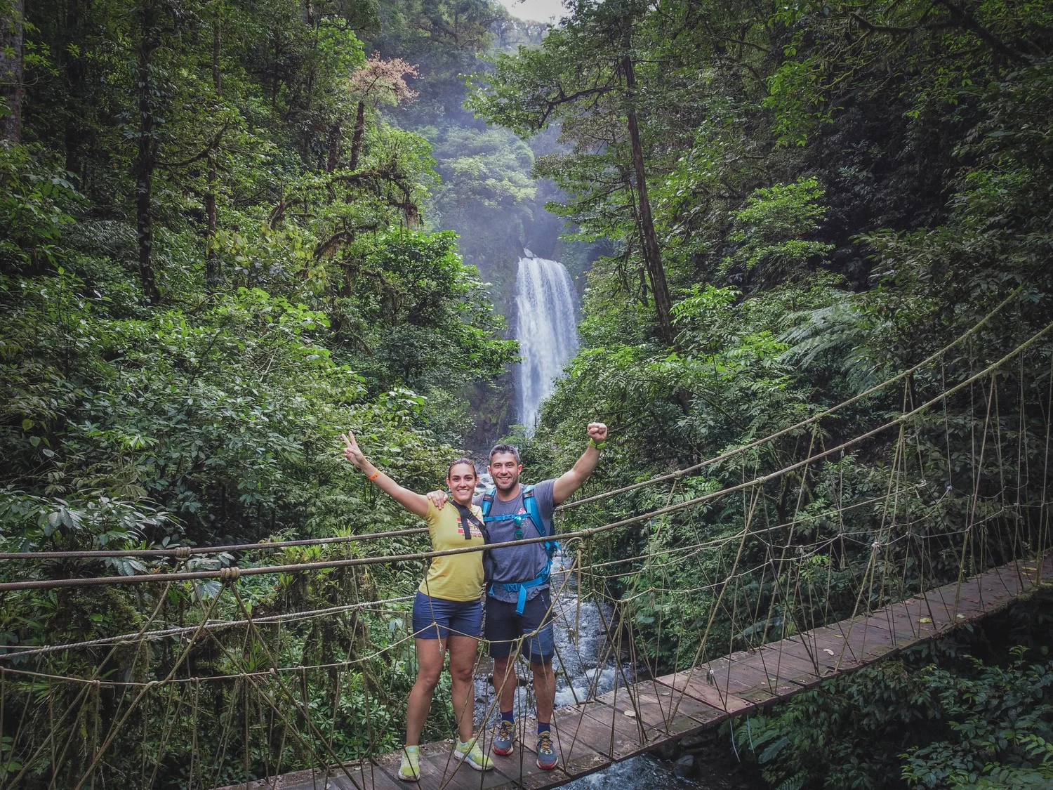 Happy couple posing on a suspension bridge with the majestic El Tigre Waterfalls in Monteverde, Costa Rica.