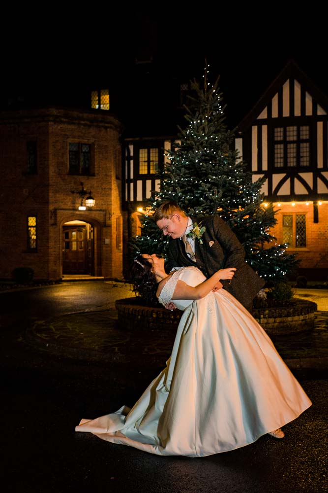 Bride and groom embraced infront of a Christmas tree.