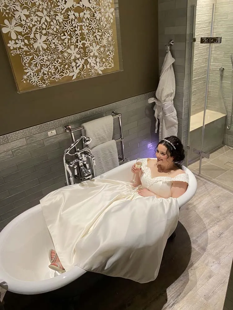 A bride in full wedding attire sitting in the bath of her bridal suite.