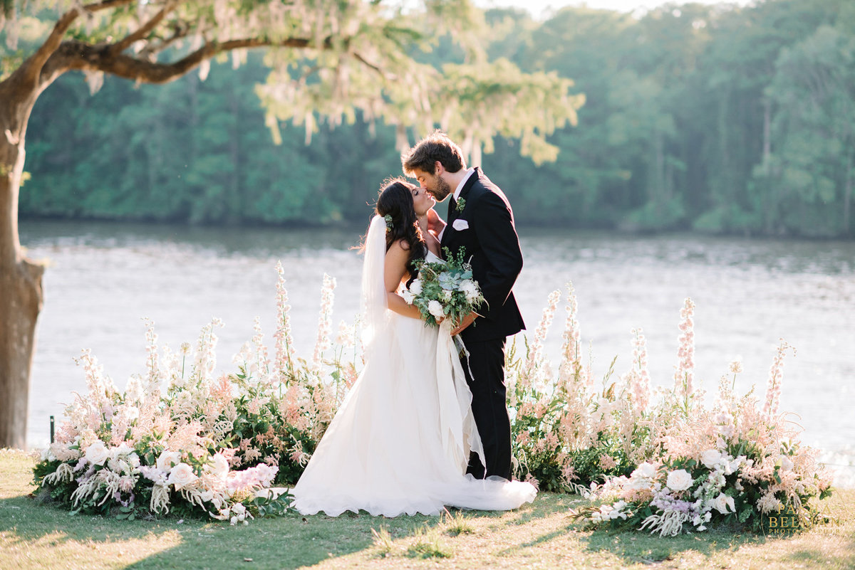 A bride and groom by a lake kissing