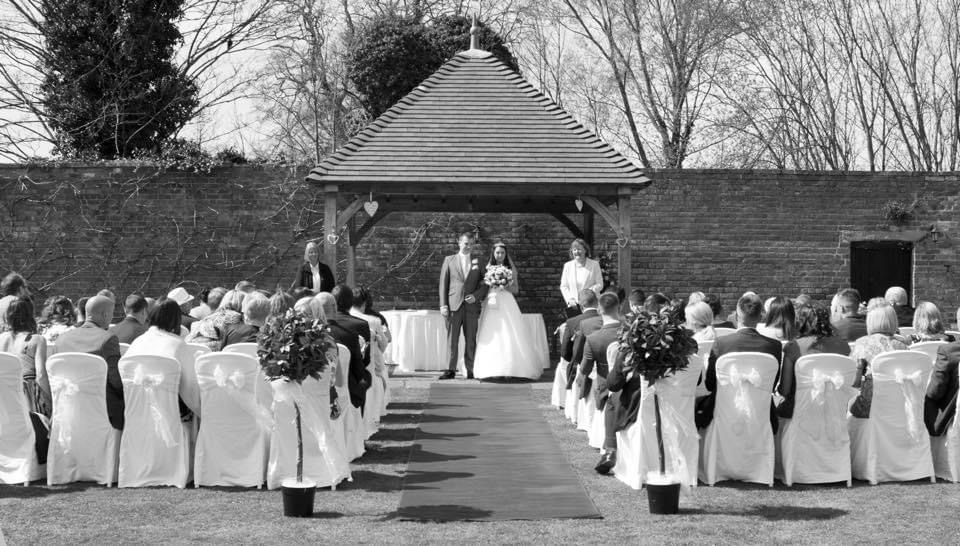 Bride and Groom having their wedding ceremony in the walled garden at Hatherey Manor Gloucester.
