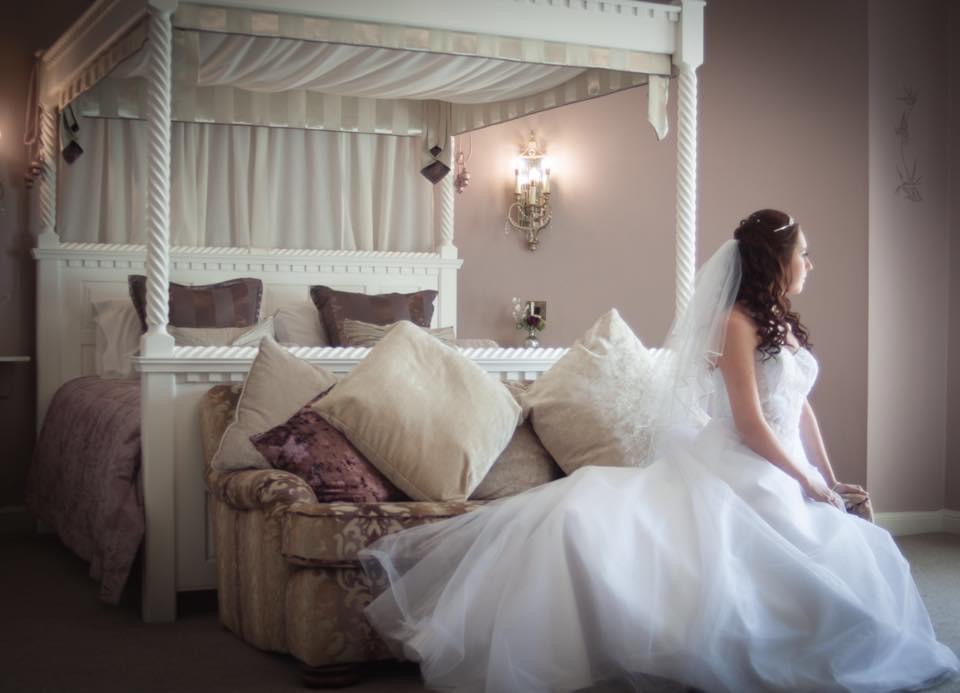 A brides seated at the foot of a four poster bed ready for her ceremony.