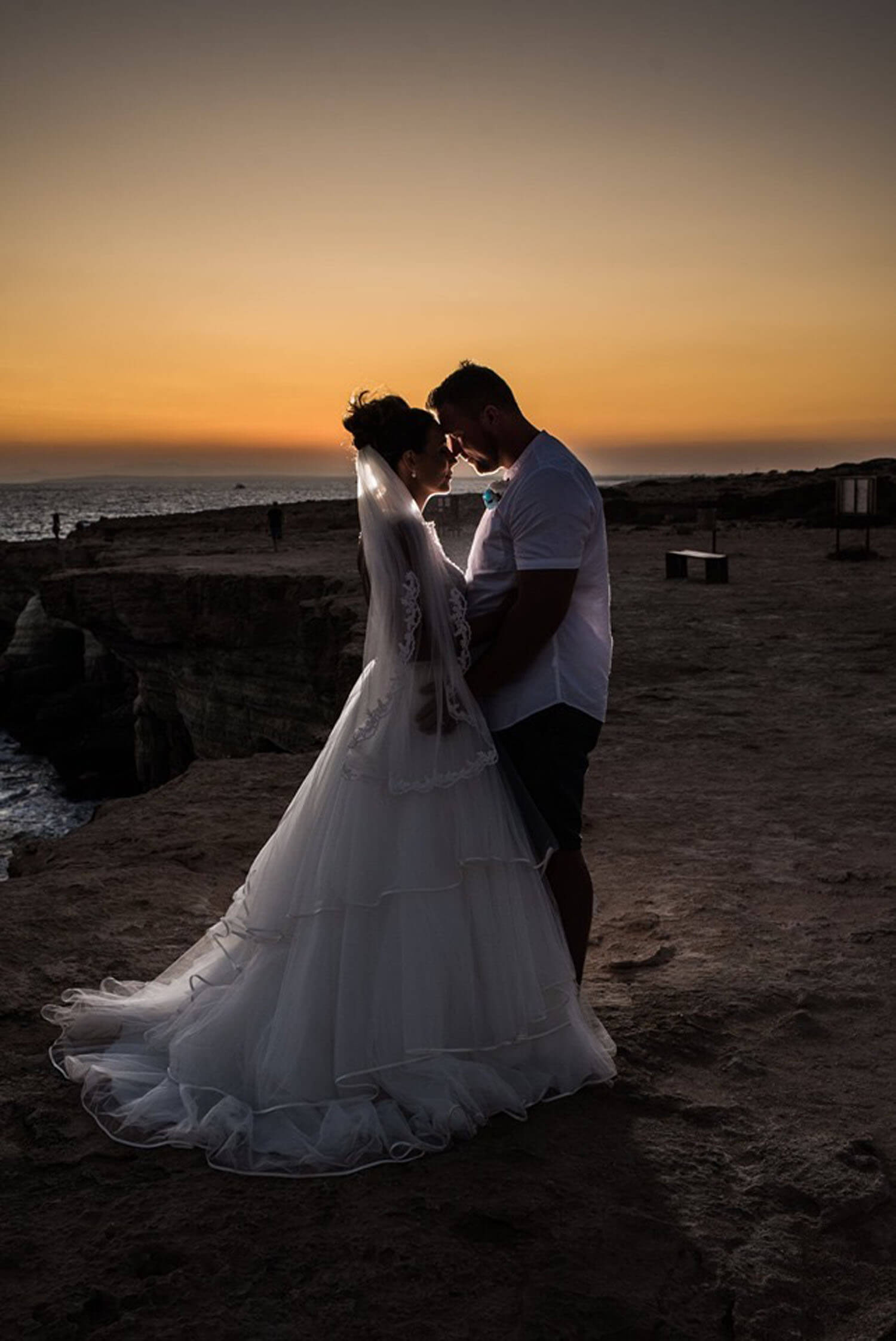 Bride and Groom standing near the sea at sunset.