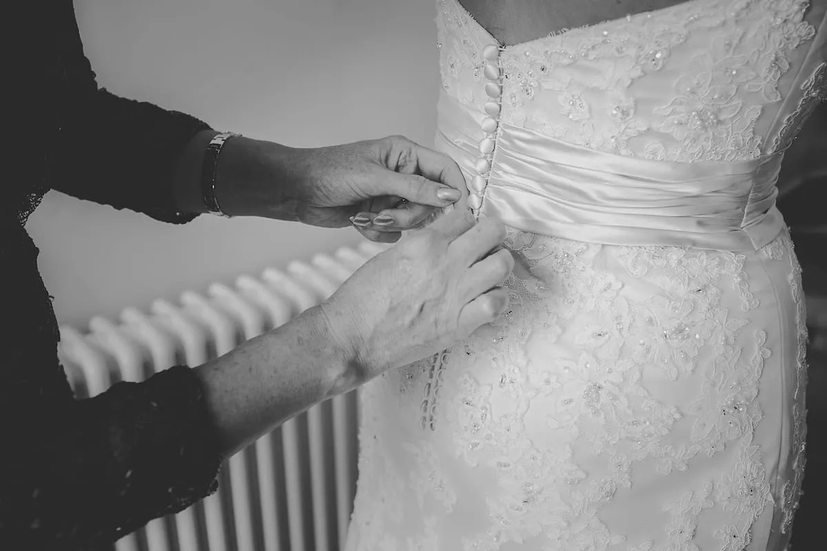 Bride being fastened into her buttoned back wedding dress 