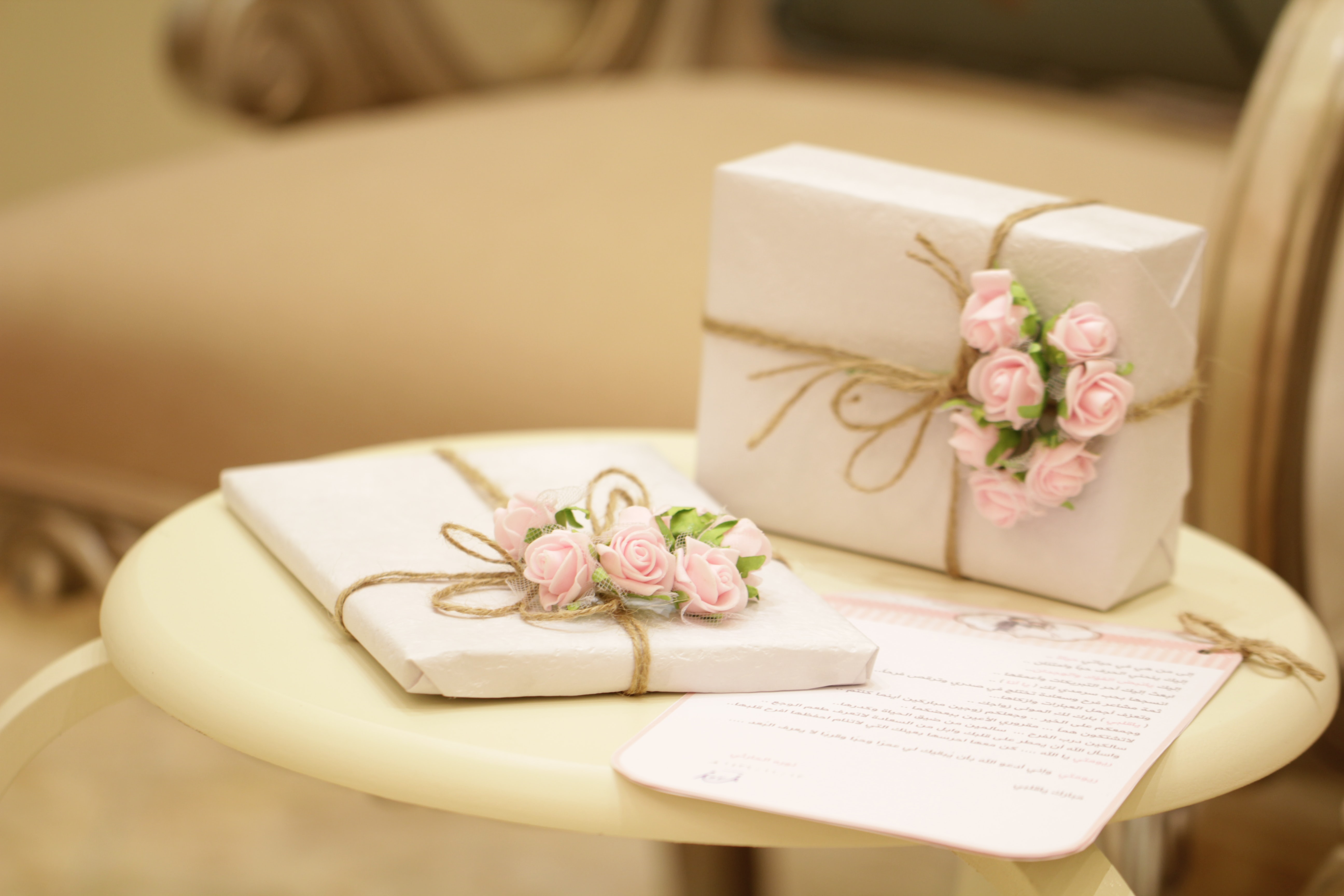A pair of wedding gifts wrapped in paper and tied with string with tiny pink roses.