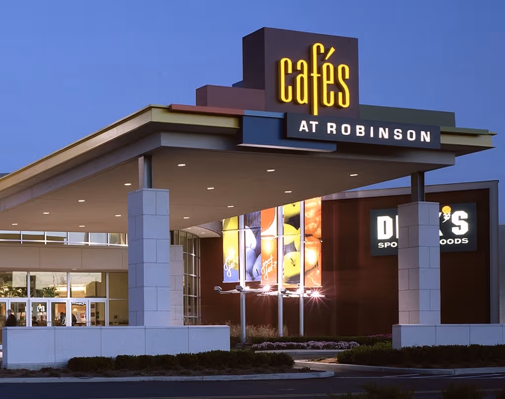 Entrance canopy of Cafés at Robinson mall illuminated in evening light with signs and glass doors.