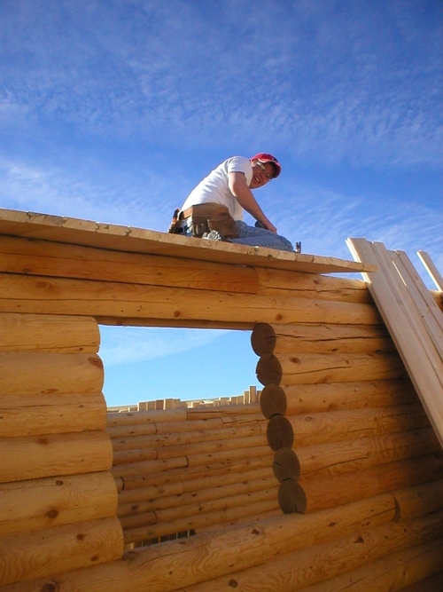 Image of worker on the roof of a cabin that's under construction