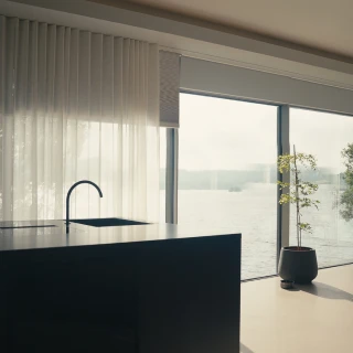Modern kitchen interior with black island, minimalist faucet, sheer curtains, and large glass door overlooking water.