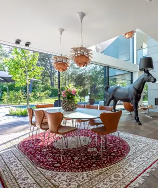 Modern dining area with round table, brown chairs, floral centerpiece, and black dog-shaped floor lamp.