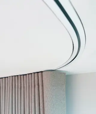 Curved white ceiling recess with concealed strip light above a textured wall and brown curtains.