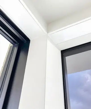 Corner of a white ceiling with black-framed windows showing a blue sky with clouds.