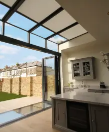 Modern kitchen with glass roof, large open window, and view of backyard with brick wall.