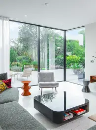 Modern living room with glass corner window showing lush green garden outside.