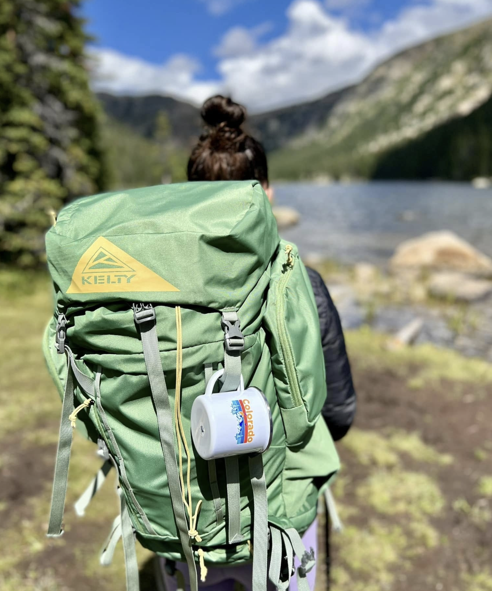 Theresa standing at the edge of a glacier lake, looking out at the mountain landscape, with backpacking gear on