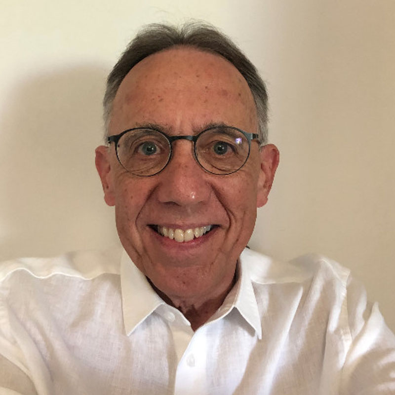Smiling middle-aged man wearing glasses and a white button-up shirt against a plain background.