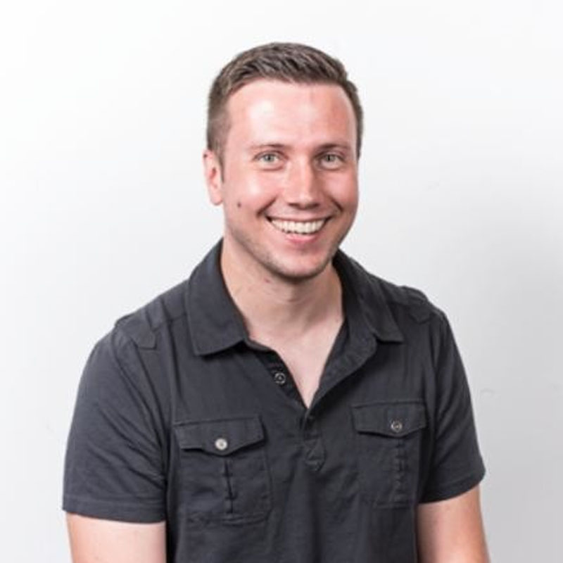 Smiling man in a short-sleeve black button-up shirt against a plain white background.