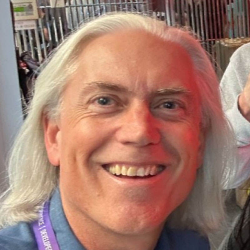 Close-up of a smiling middle-aged man with long white hair and light blue eyes.